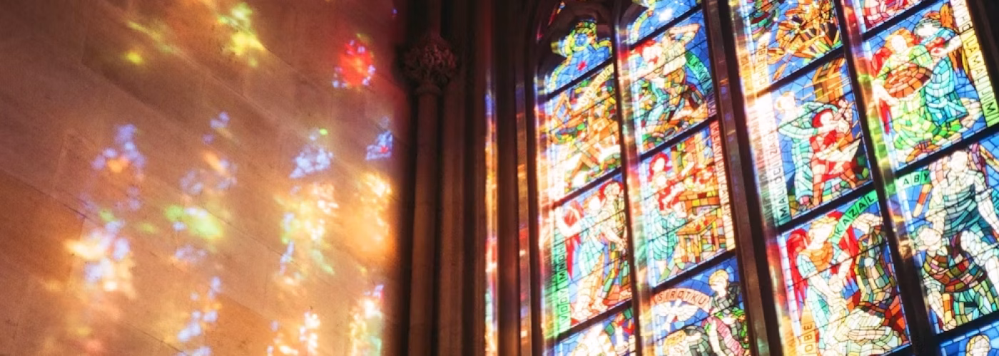 Sunlight refracting through stained glass onto a stone wall inside a church.